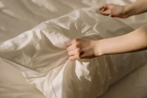 Manos arreglando una funda de almohada blanca, como si se preparara para blanquear fundas de almohadas amarillentas.