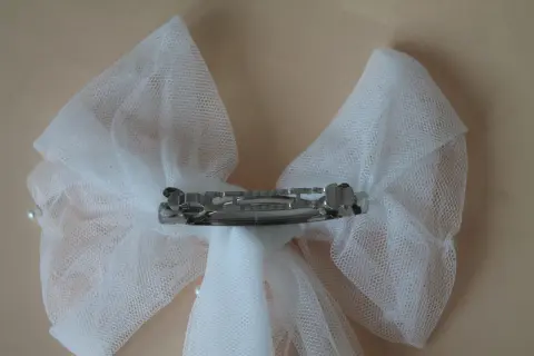 Un delicado lazo de tul blanco, adornado con perlas, sujeto por una pinza plateada.