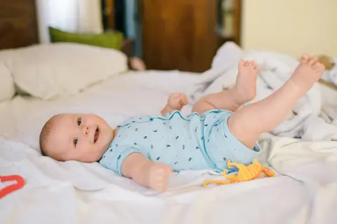 Mi bebé de 2 meses se voltea, sonriendo y jugando con un dinosaurio de juguete en la cama.