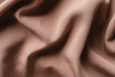 Textura de tela de satén color caramelo con pliegues suaves y sombras profundas. El satén se arruga, creando un efecto visual interesante.