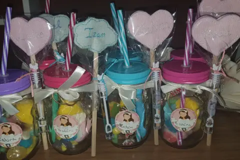 Frascos de comunión con dulces, pajitas y adornos de corazón con nombres.