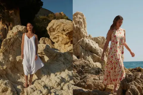 Mujer con vestido blanco de 100% viscosa y otro con estampado de coral, posando en rocas junto al mar.