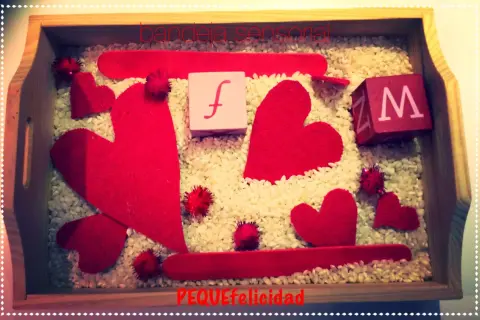 Bandeja sensorial de San Valentín para niños con corazones rojos, cubos con letras y arroz.