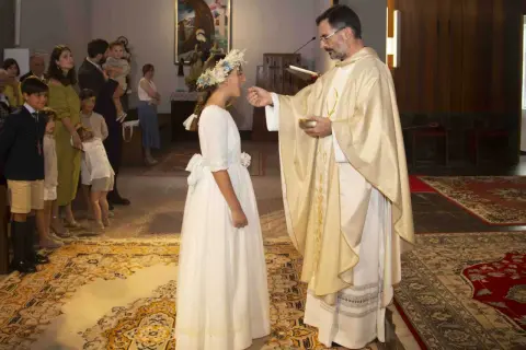 Niña recibe la comunión, un momento especial que marca a qué edad se hace la comunión. Familiares observan.