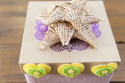 Caja de regalo decorada con un lazo grande de tela, corazones y un diseño floral.