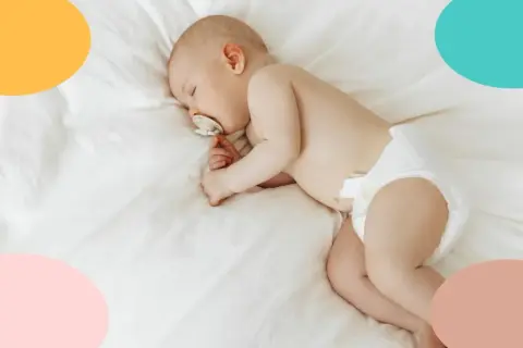 Un tierno bebé duerme de lado, con un chupete en la boca, envuelto en una suave manta blanca.