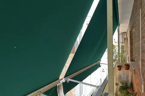 La lona verde protege del sol en un balcón con ladrillos.