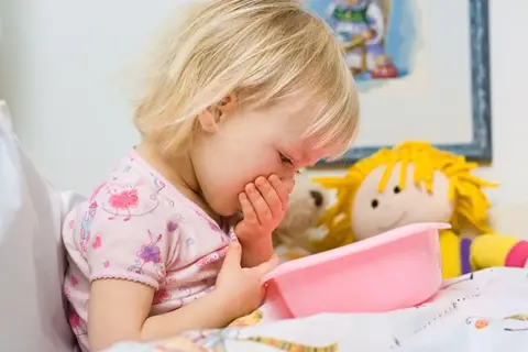 Niña rubia con vómito, posiblemente por rotavirus en niños. Sostiene un recipiente rosa.