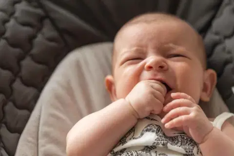 Un bebé de 3 meses intenta incorporarse, con su mano en la boca, en una hamaca acolchada.