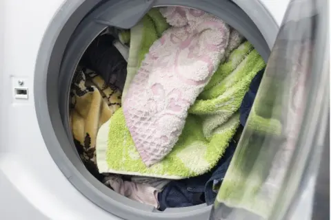 Interior de lavadora con ropa variada: toallas verdes y rosas, mantas y prendas oscuras. ¿Cuánto tiempo puede estar la ropa en la lavadora?