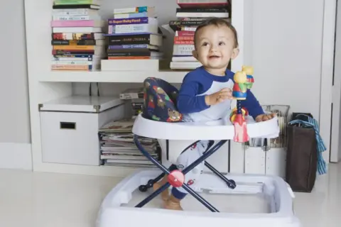 Bebé sonriente en andador, rodeado de libros. Posibles consecuencias del uso del andador en bebés.