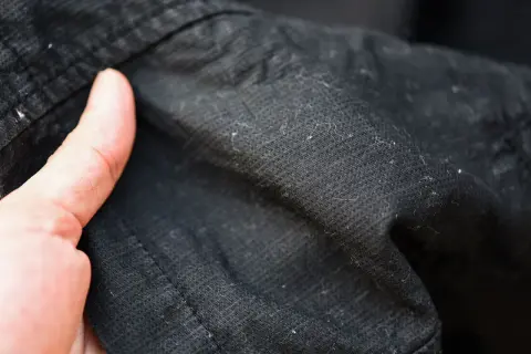 Dedos señalan motas negras en ropa oscura, resultado de la lavadora.