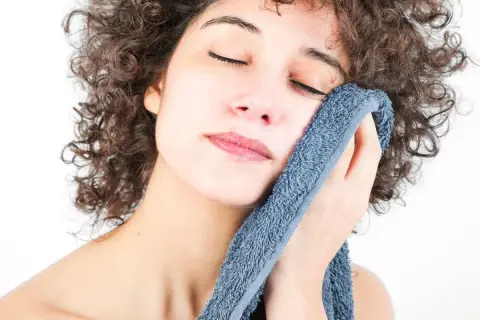 Mujer con rizos oscuros se seca la cara con toallas suaves y con buen olor, disfrutando de un momento de frescura.