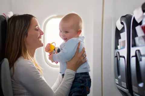 Madre sonríe a su bebé en un avión, jugando con un sonajero. Viajar con bebés puede ser una aventura alegre.