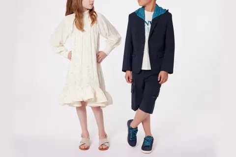 Niño y niña posan con atuendos elegantes. Ideas para como vestir a un niño de 14 años para una boda: traje azul marino con capota y bermudas.