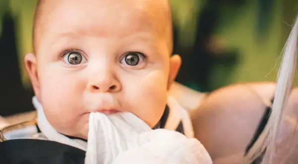Ojos de bebés antes y después: un primer plano de un bebé con ojos curiosos y una tela blanca en la boca.