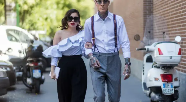 Pareja elegante camina, él es un invitado boda hombre sin traje, con tirantes y tatuajes visibles.
