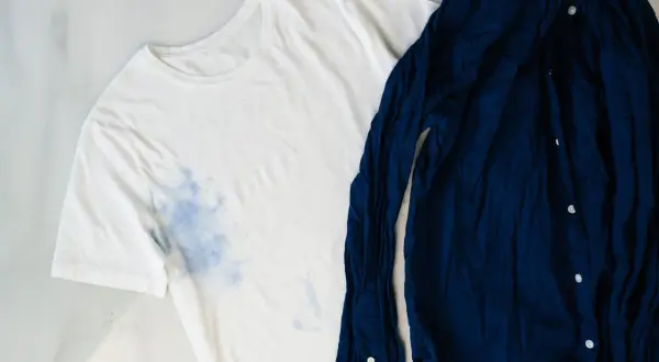 Camiseta blanca con manchas azules y camisa azul marino. Aprende como quitar el desteñido de la ropa de color.