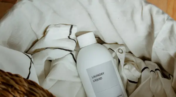 Botella de detergente para ropa en una cesta con ropa de lino. Aprende como lavar el lino para que no encoja.