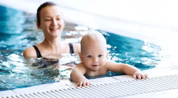 Un bebé sonriente disfruta de la natación con su madre en una piscina.