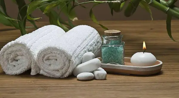 Toallas blancas enrolladas, sales de baño azules, vela encendida y bambú, ideal para recuperar toallas ásperas y disfrutar de un momento de spa.