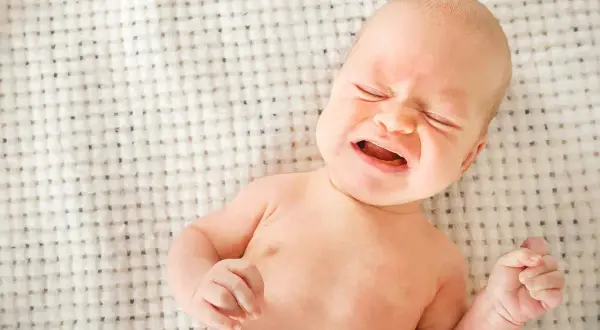 Bebé llorando, con ojos cerrados y boca abierta. Podría ser uno de los signos de deshidratación en bebés.