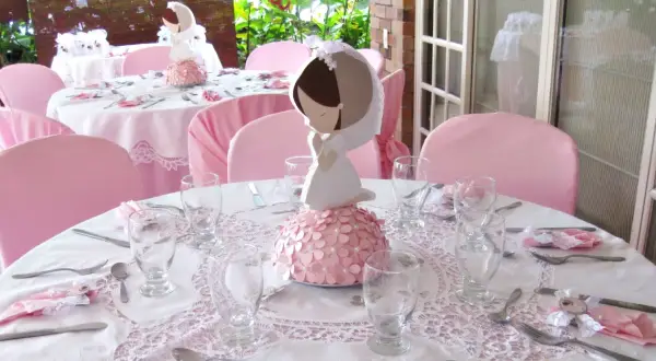 Detalle de decoración comunión niña casera con centros de mesa de comunión y mesas vestidas de rosa.