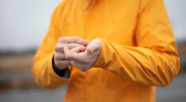 Persona ajustando la manga de su chaqueta naranja de poliéster.