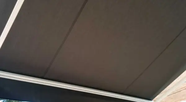 Toldo de acrílico tela oscura, con estructura blanca, protegiendo del sol.