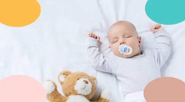 Bebé de 4 meses duerme de lado con chupete y osito.