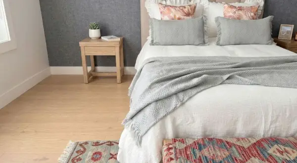 Cama acogedora con colcha de lino que da calor. Cojines grises y alfombra de estilo étnico.
