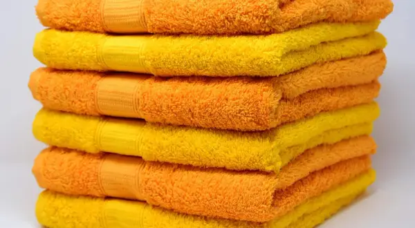 Pila de toallas suaves y esponjosas en tonos naranja y amarillo, listas para un baño reconfortante.