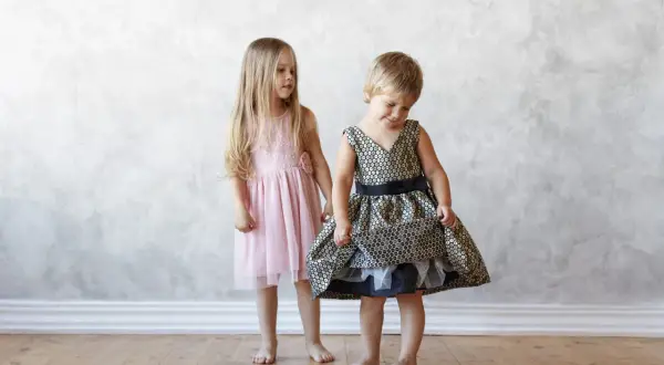 Dos niñas, una con un vestido rosa y otra con uno dorado y negro, muestran la ropa que llevan los niños en una boda.