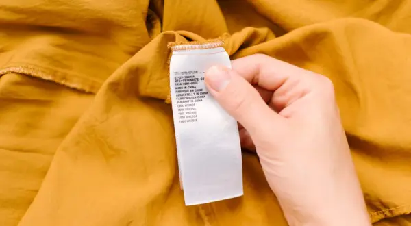 Etiqueta de cuidado de una prenda de color mostaza. Indica "100% viscosa", advirtiendo que la viscosa encoge si no se cuida.