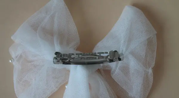 Un delicado lazo de tul blanco, adornado con perlas, sujeto por una pinza plateada.