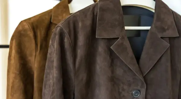 Dos chaquetas de ante, una marrón y otra café, colgadas en perchas. ¿Sabías que se puede lavar una chaqueta de ante en la lavadora?