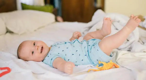 Mi bebé de 2 meses se voltea, sonriendo y jugando con un dinosaurio de juguete en la cama.