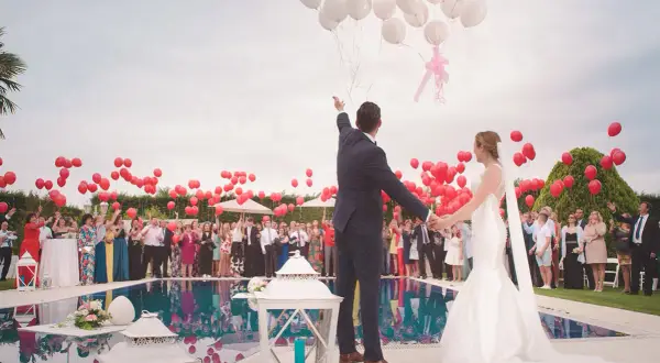 Novios liberando globos en una boda, rodeados de invitados y niños.