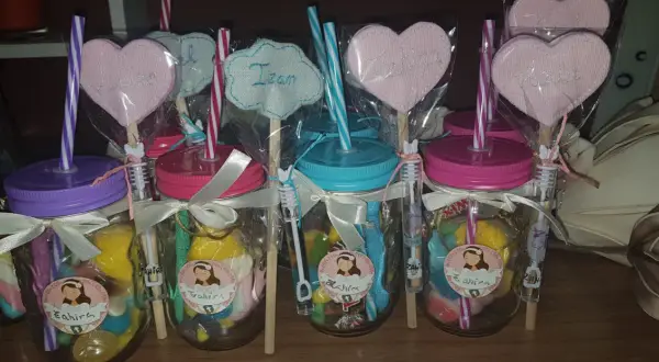 Frascos de comunión con dulces, pajitas y adornos de corazón con nombres.