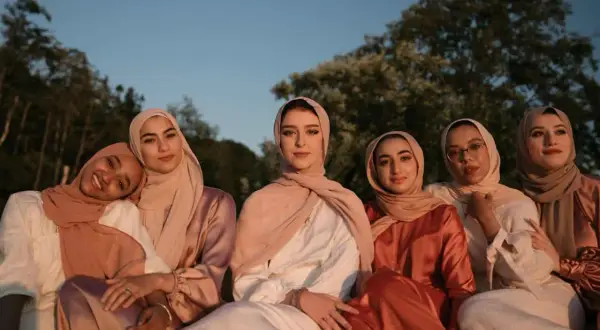 Seis mujeres con hiyabs posan juntas. El tejido modal se arruga suavemente en sus vestidos, creando un efecto elegante bajo la luz del atardecer.