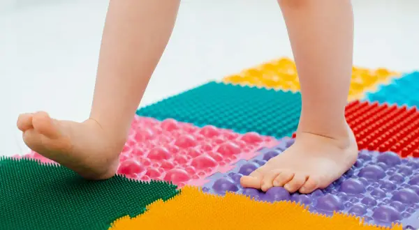 Niño camina sobre un tapete terapéutico de colores para fortalecer sus pies planos.