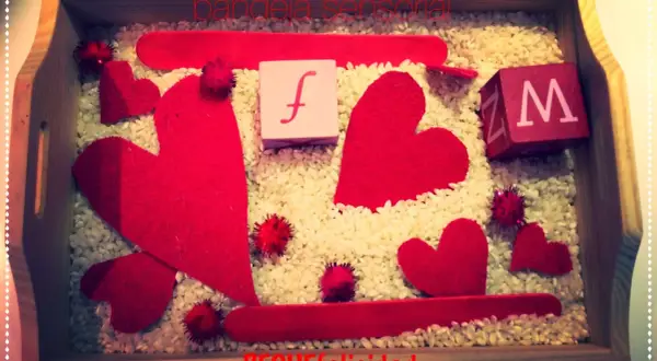 Bandeja sensorial de San Valentín para niños con corazones rojos, cubos con letras y arroz.