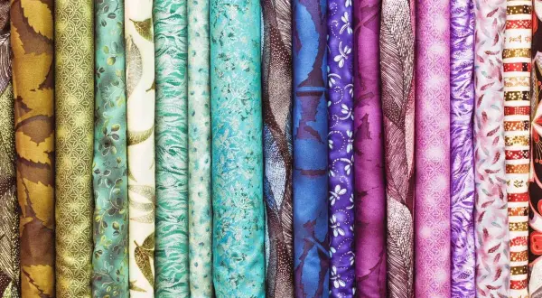 Variedad de telas enrolladas, con estampados florales, de hojas y abstractos en tonos verdes, azules y morados. La gasa se mezcla con otros tejidos.
