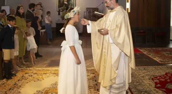 Niña recibe la comunión, un momento especial que marca a qué edad se hace la comunión. Familiares observan.