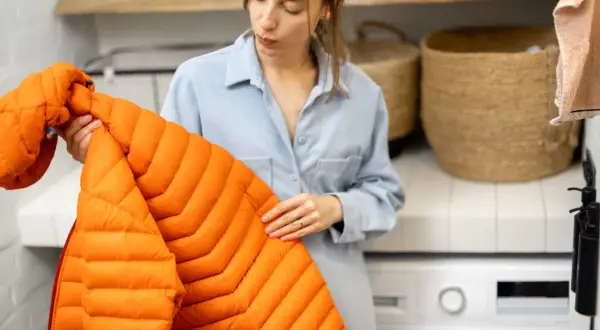 Mujer revisa un abrigo naranja, pensando cómo secar un plumas sin secadora.