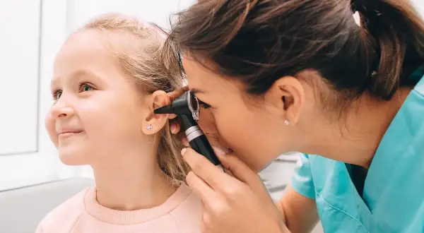 Médico examina el oído de una niña con otoscopio. Una revisión para descartar otitis en niños.