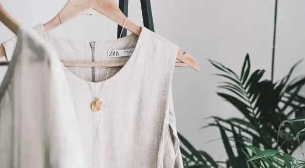 Vestido de lino beige colgado en percha, con collar dorado. Descubre trucos para que no se arrugue el lino y mantén tu ropa impecable.