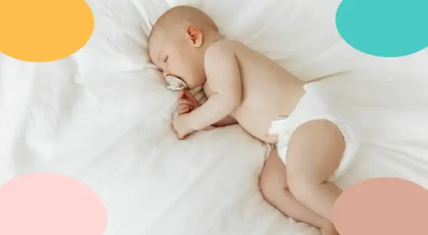 Un tierno bebé duerme de lado, con un chupete en la boca, envuelto en una suave manta blanca.