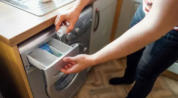 Persona vierte detergente en la lavadora para que la ropa acartonada quede limpia y suave.