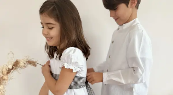 Hermanos de comunión, un niño ayuda a su hermana a ajustar el lazo de su vestido blanco, preparándose para un día especial.